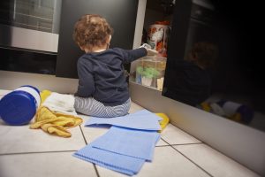 Baby boy opens up kitchen cupboard and pulls out various cleaning products from under the sink while his parents are distracted