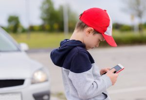 Child busy playing the smartphone mobile games does not pay attention to the moving car. Boy child playing mobile games on smartphone on the street