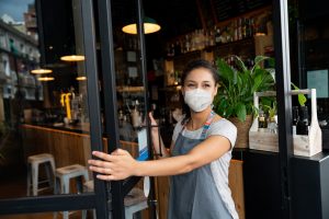 Feliz propietario de un negocio abriendo la puerta de un café con una máscara facial para evitar la propagación del coronavirus, reabriendo después de los conceptos de COVID-19