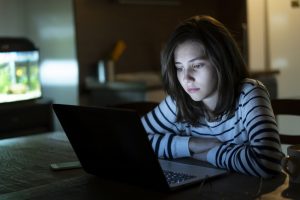 Young girl is reading alone on her laptop late at night