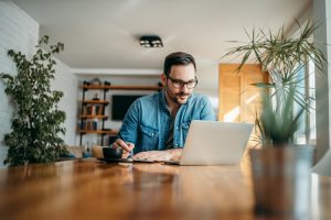 Hombre tomando notas y mirando la computadora portátil, en la oficina en casa, retrato.