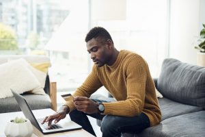 Shot of a young man using a laptop and credit card at home