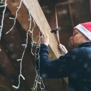 man with santa hat decorating house outdoor carport with christmas string lights