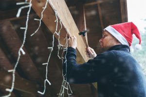 hombre con sombrero de santa decorando casa cochera al aire libre con luces de cadena de navidad