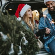 Happy couple is wearing Santa Claus hat and sitting in car trunk while enjoying their beautiful moments of Christmas tree adventure. It is a cold and sunny day outside.