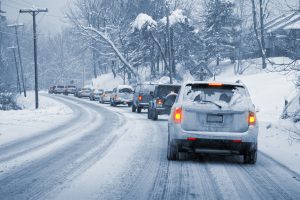 Una hilera de coches circulando lentamente por una carretera cubierta de nieve y hielo.  Toda la imagen es azul monocromática, excepto las luces traseras, que brillan en rojo y amarillo.