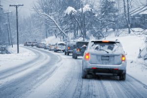 A line of cars slowly driving on a snowy, icy road. Entire image is monochrome blue-ish except the taillights, which are glowing red and yellow.