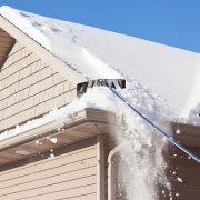 A roof rake is being used to remove snow from a winter roof. Large amounts of snow are often removed, using this method, to prevent ice dams and reduce excess weight. Ice dams form when melted roof snow freezes at the gutter sometimes leading to damage to the roof edge.