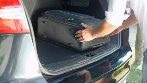 Person putting travel bags in a car trunk