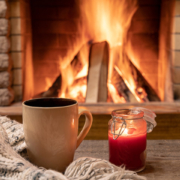 Big mug with hot tea and a candle, wool scarf, near cozy fireplace, in country house